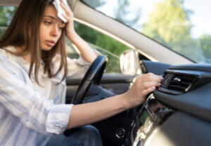 Woman suffering for excessive heat turning on AC in her car.